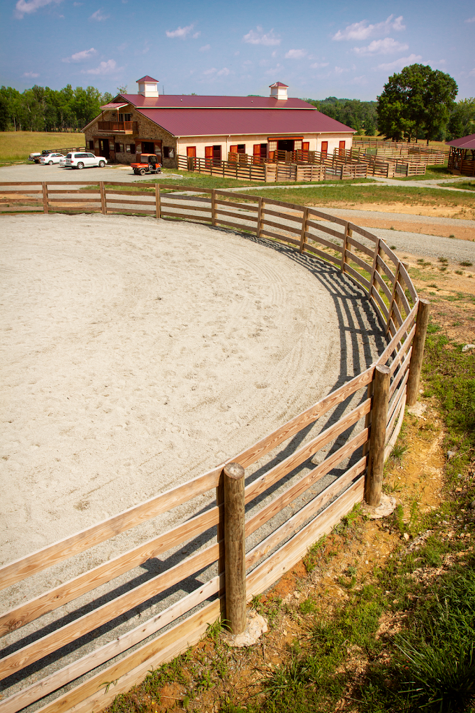 The outdoor round pen with the main barn beyond under a clear sky