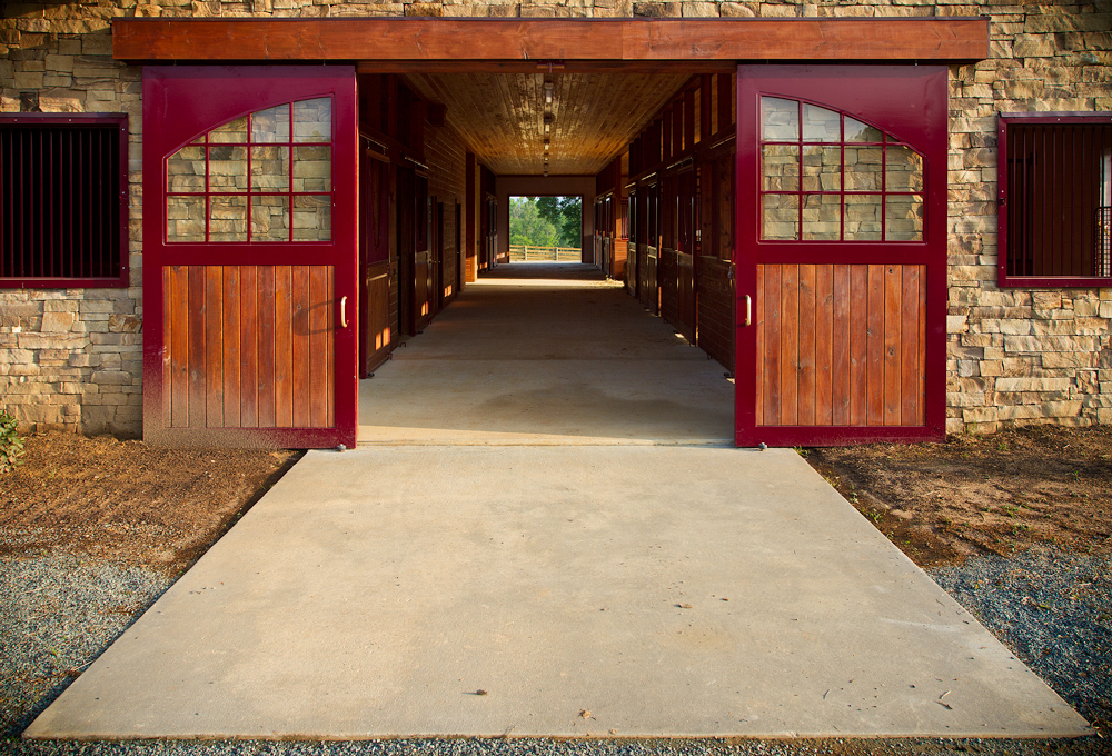 The interior aisle of the barn—open red doors, stone walls, and stalls along a central walkway