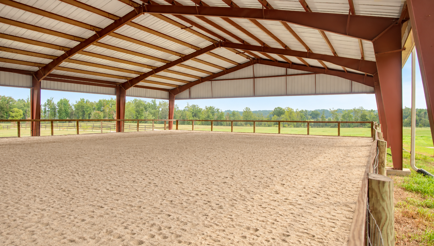 The covered arena—open-sided, bright, with sand footing and a clear view of the fields beyond